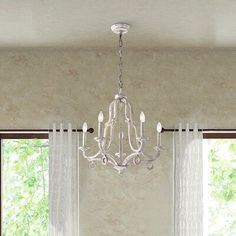 a chandelier hangs from the ceiling in front of a window with sheer curtains