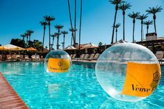 two inflatable balls floating on top of a swimming pool next to palm trees