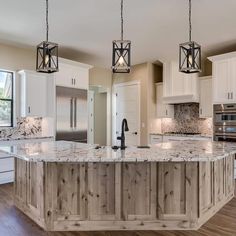 a large kitchen with an island in the middle and two pendant lights hanging from the ceiling