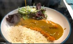 a white plate topped with rice and meat covered in gravy on top of a table