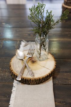 a fork and spoon sitting on top of a wooden table next to a jar filled with greenery