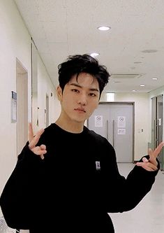 a young man standing in a hallway making the peace sign with his hands while wearing a black shirt