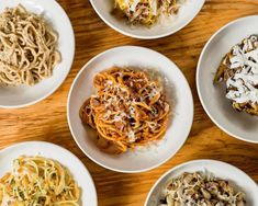 four white plates with different types of food on top of a wooden table next to each other