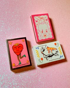 two small boxes with designs on them sitting next to each other in front of a pink background