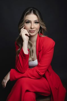 a woman sitting on top of a wooden table wearing a red suit and white shirt