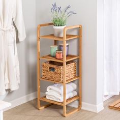 a bamboo shelf with baskets and towels on it next to a bathrobe in a bathroom