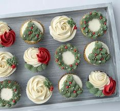 twelve cupcakes decorated with white frosting and holly wreaths are arranged in a box