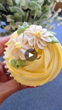 a cupcake with yellow frosting and white flowers on it is being held by someone