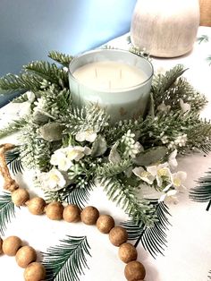 a candle is sitting on a table with flowers and greenery around it, next to a bead necklace