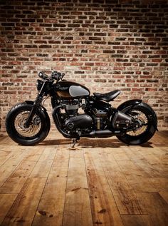 a black motorcycle parked on top of a wooden floor next to a brick wall in an empty room