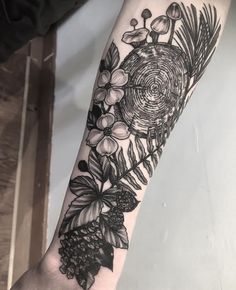 a black and white flower tattoo on the left arm with pine cones, berries and leaves