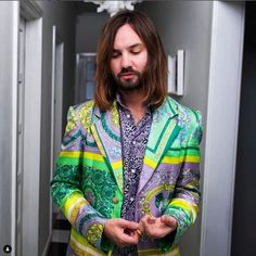 a man with long hair wearing a colorful suit and looking down at his cell phone