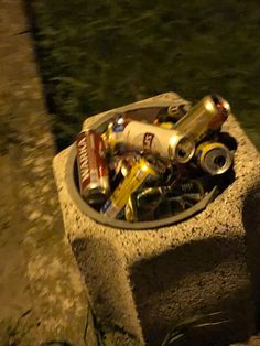 an assortment of beer cans and batteries in a cement container on the side of a road