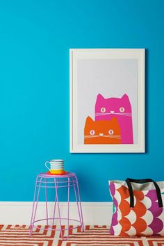 a cat print hangs on the wall next to a pink and orange bag, with a blue background