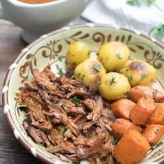 a bowl filled with meat, potatoes and carrots on top of a wooden table