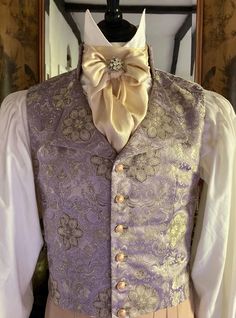 Mens single breasted Regency style waistcoat made in an opulent lilac, gold and silver brocade in an eye catching floral design, six gold tone filigree buttons, stand collar with shaped lapels. The sumptuous fabric is a lavish lilac, gold and silver brocade in an eye catching floral design, the metallic threads catch the light wonderfully, the fabric is absolutely perfect for the Regency period. It will look stunning for a Regency Ball, Bridgerton Event, Regency Wedding, The Jane Austen Festival. Six unusual filigree gold tone buttons to the front of the waistcoat, which add that extra luxurious period detail and also catch the light beautifully. The waistcoat is backed in a ivory coloured medium weight cotton. The waistcoat is fully lined in antique gold satin. The chest will fit up to 38 Elegant Party Vest With Buttons, Elegant Wedding Vest With Buttons, Sleeveless Vest With Buttons For Wedding, Fitted Wedding Vest With Buttons, Fitted Vest With Buttons For Wedding, Fitted Gold Vest Elegant Style, Elegant Gold Fitted Vest, Gold Fitted Vest, Fitted Gold Elegant Vest