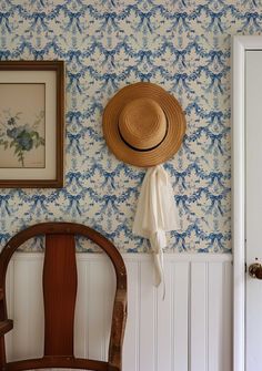 a hat is hanging on the wall next to a wooden chair and framed painting in a room