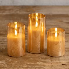 three gold colored candles sitting on top of a wooden table next to eachother