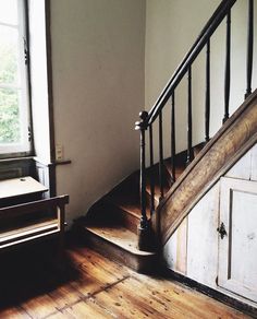 an old wooden stair case next to a window in a room with wood floors and white walls