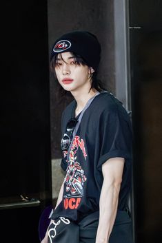 a young man wearing a black shirt and hat standing in front of a door with his hand on his hip