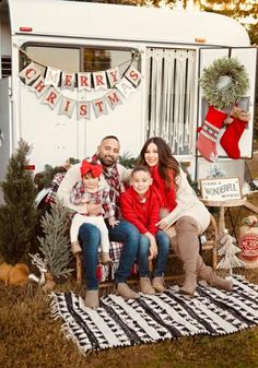 a family sitting on a bench in front of a trailer decorated with christmas stockings and garlands