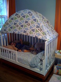 two children sleeping in a crib with an umbrella on top of the cotter