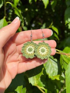 a pair of green earrings is shown in front of some leaves and bushes, with the sun shining on them