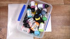 a plastic container filled with lots of different types of paint and markers on top of a piece of paper