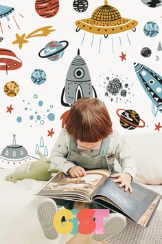 a young child is reading a book in front of a wall with space themed decals