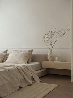 a white bed sitting next to a wooden table with a vase on top of it