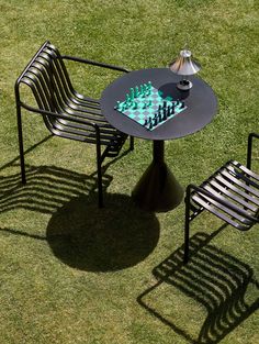 two chairs and a table with chess pieces on it sitting in the grass next to each other