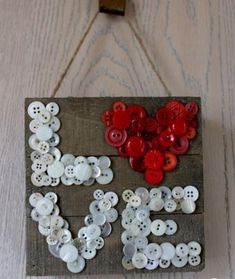 a piece of wood with buttons on it hanging from a hook that says love spelled out in white and red