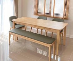 a wooden table with four green chairs and a bench in front of the window that has blinds on it