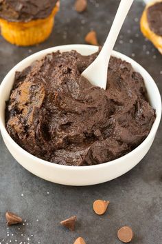 a white bowl filled with chocolate frosting next to cupcakes