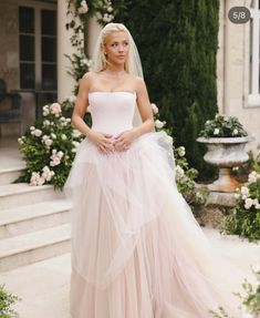 a woman in a wedding dress is standing on the steps with her hands behind her back