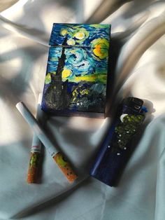 three different colored pens are laying on a white sheet next to an art book with the painting starry night