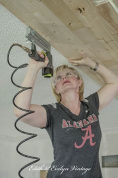 a woman is working on the underside of a wooden ceiling beam with power tools attached to it