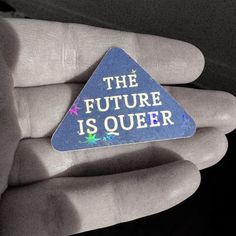 a hand holding a blue triangle shaped pin with the words the future is queen on it