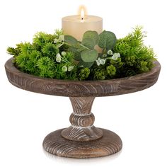 a candle sits on top of a wooden stand with greenery and foliage in it