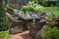 an outdoor dining set with wicker chairs and table in the middle of a garden