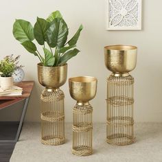 three golden metal vases with plants in them