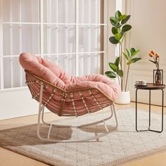 a pink chair sitting on top of a wooden floor next to a plant in a living room