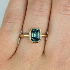 a woman's hand wearing a gold ring with an emerald stone in the center