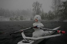 a snowman sitting on top of a kayak in the middle of a lake