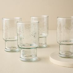 four clear glass cups sitting on top of a white table next to each other,