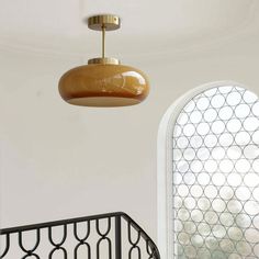 a light fixture hanging from the ceiling next to a spiral stair railing with an arched window in the background