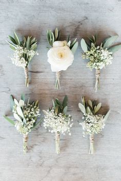 six white flowers and greenery arranged on a table