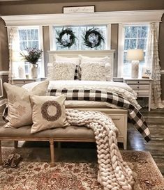 a white bed sitting in a bedroom next to two windows with wreaths on them