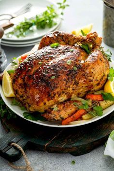 a whole chicken on a plate with lemons, carrots and parsley