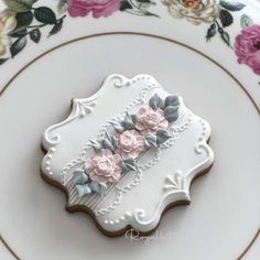 a decorated cookie sitting on top of a white and gold plate with pink flowers in the center